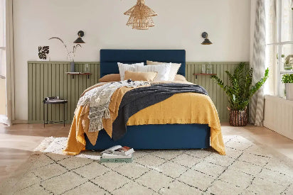 Bedroom with a bed featuring a blue headboard and yellow bedding, surrounded by decor elements.